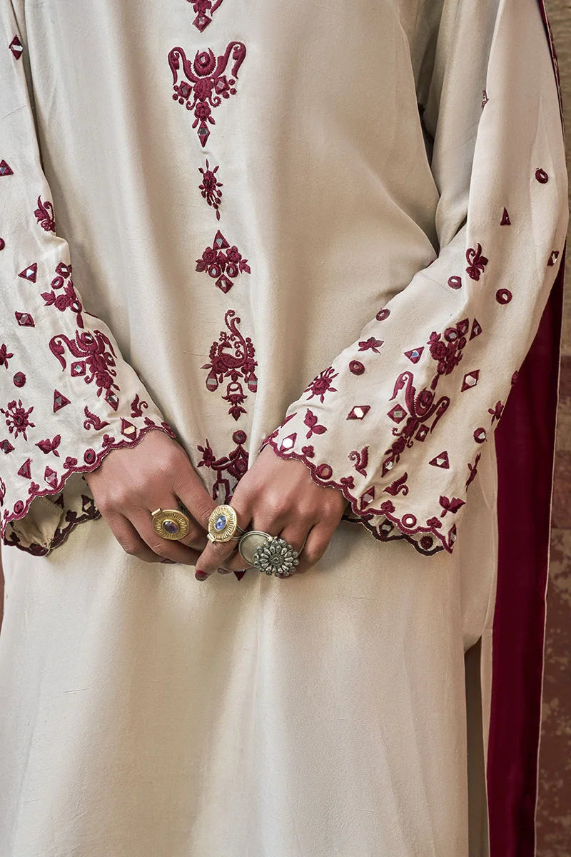 Close-up of a person wearing a cream-colored outfit with red embroidery, holding rings.