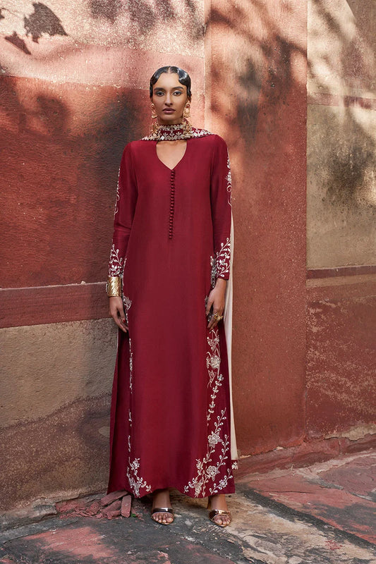 Woman wearing a red dress with white floral embroidery against a textured wall.