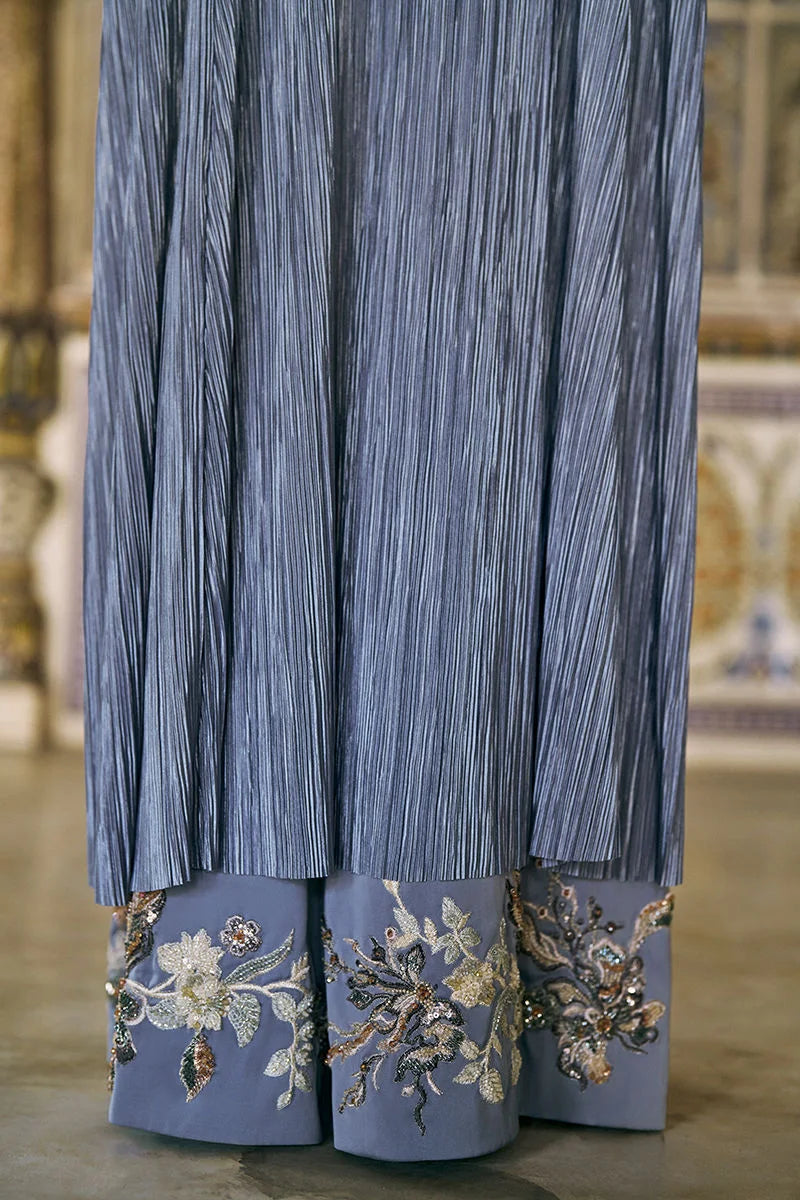 Blue pleated garment with floral embroidery on a blurred background