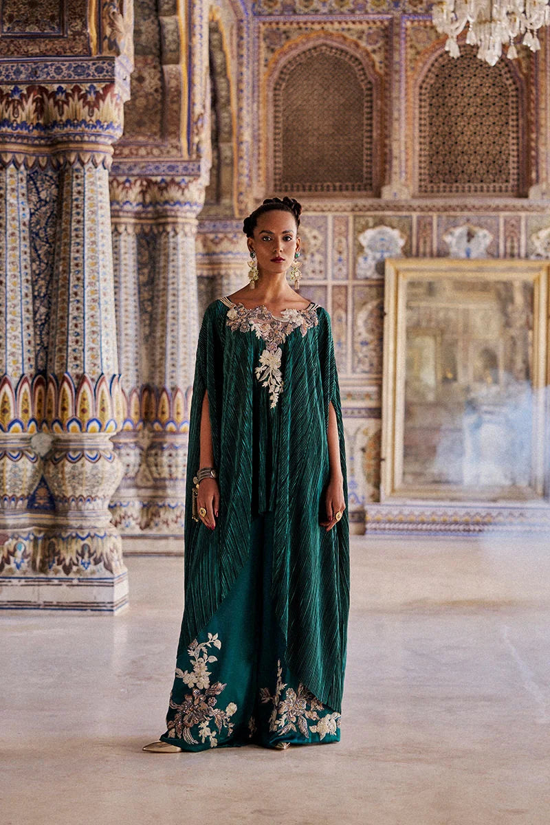 Woman in a green embroidered dress standing in an ornate room with intricate wall designs.