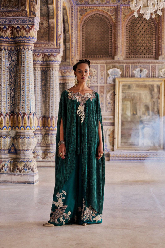 Woman in a green embroidered dress standing in an ornate room with intricate wall designs.