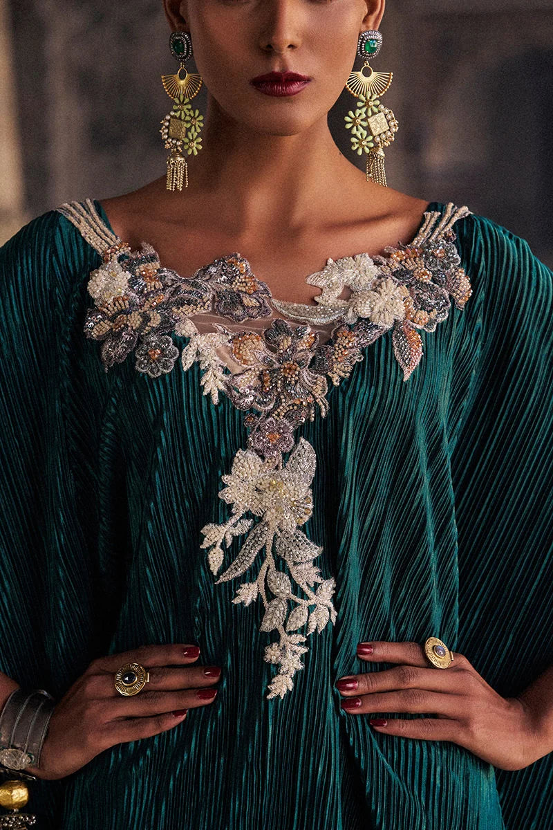 Woman wearing a teal dress with floral embroidery and gold jewelry.
