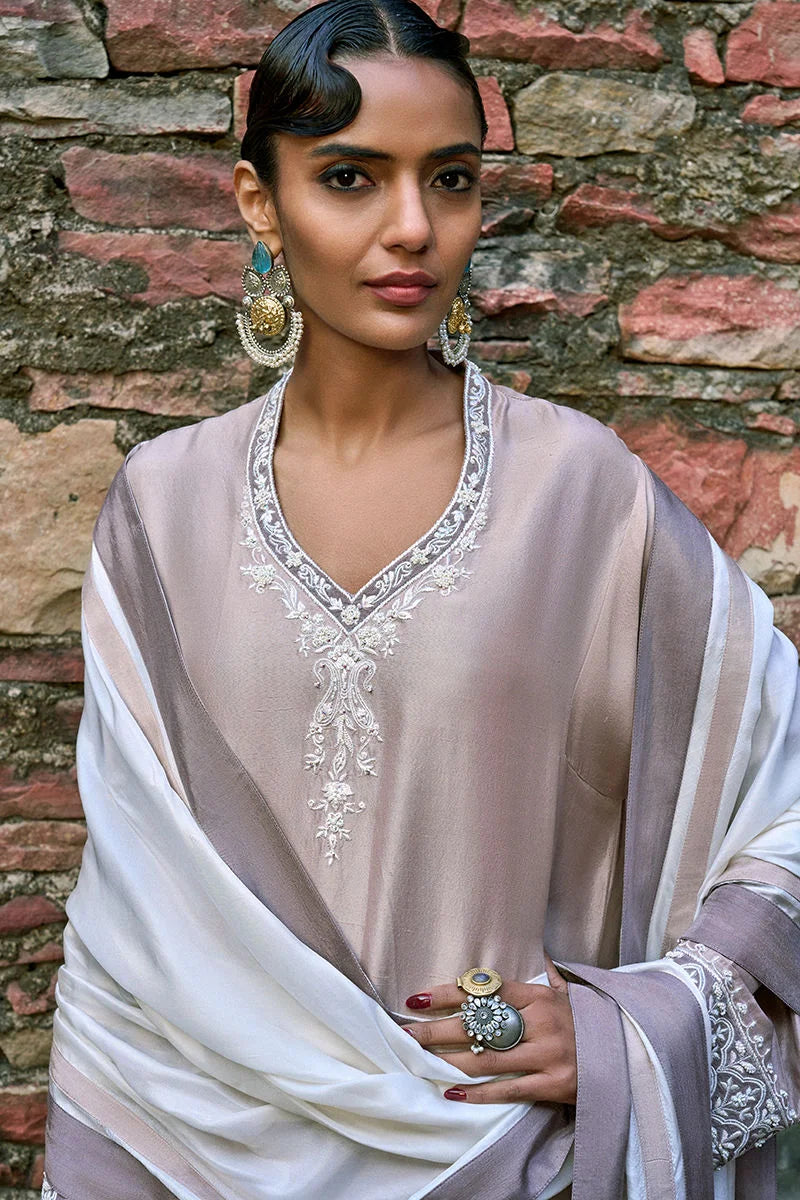 Woman wearing a traditional outfit with intricate embroidery against a stone wall.