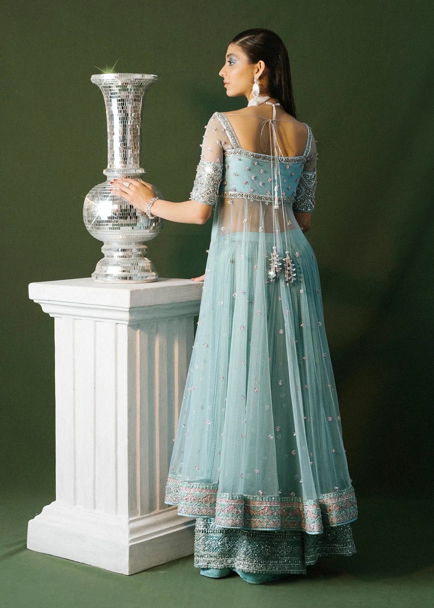 Woman in a light blue embroidered dress holding a decorative vase against a green background