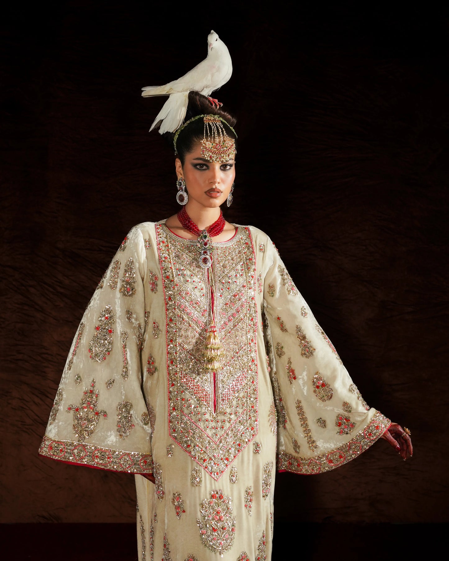 Woman in an ornate traditional outfit with a white dove on her head against a dark background