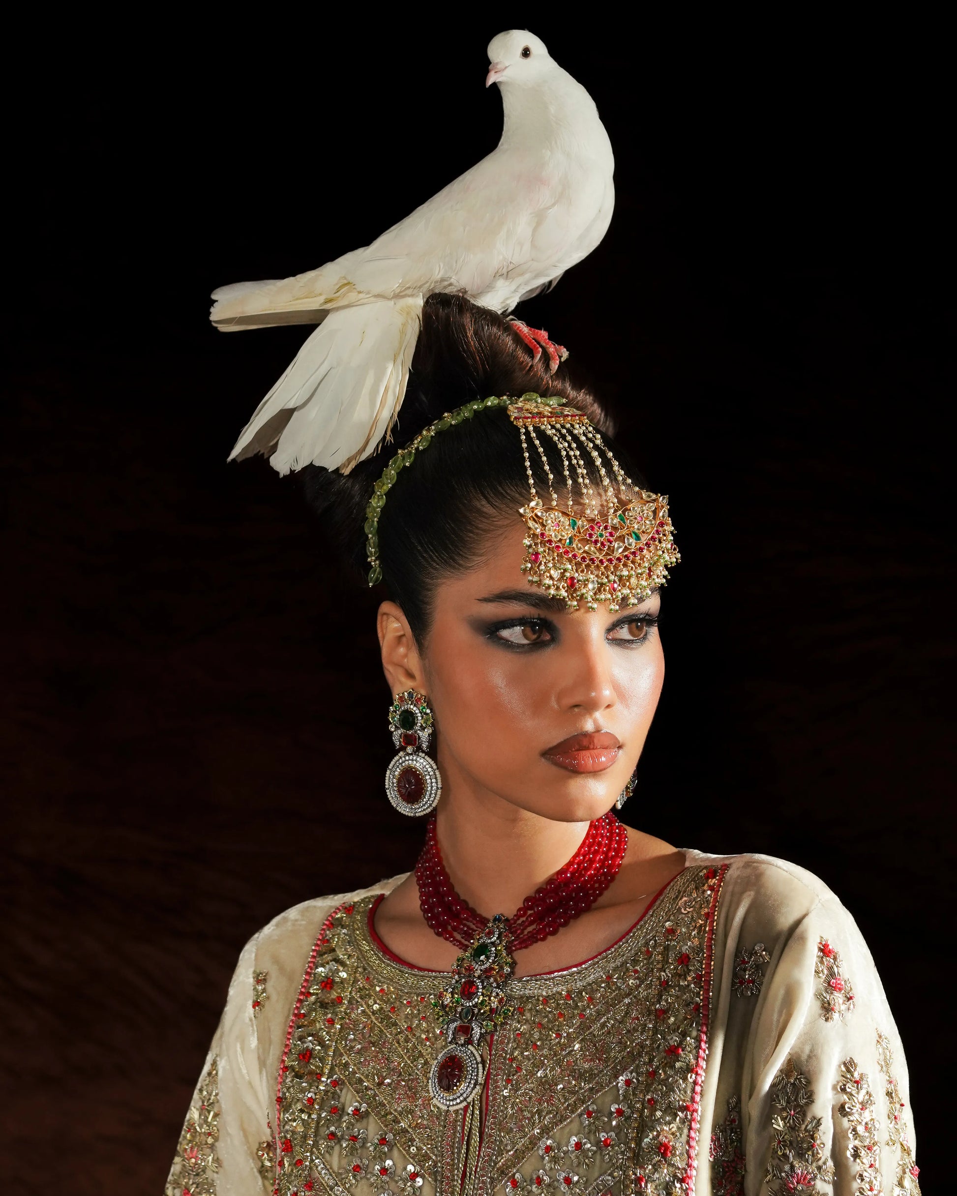 Woman in traditional attire with a white dove on her head against a dark background
