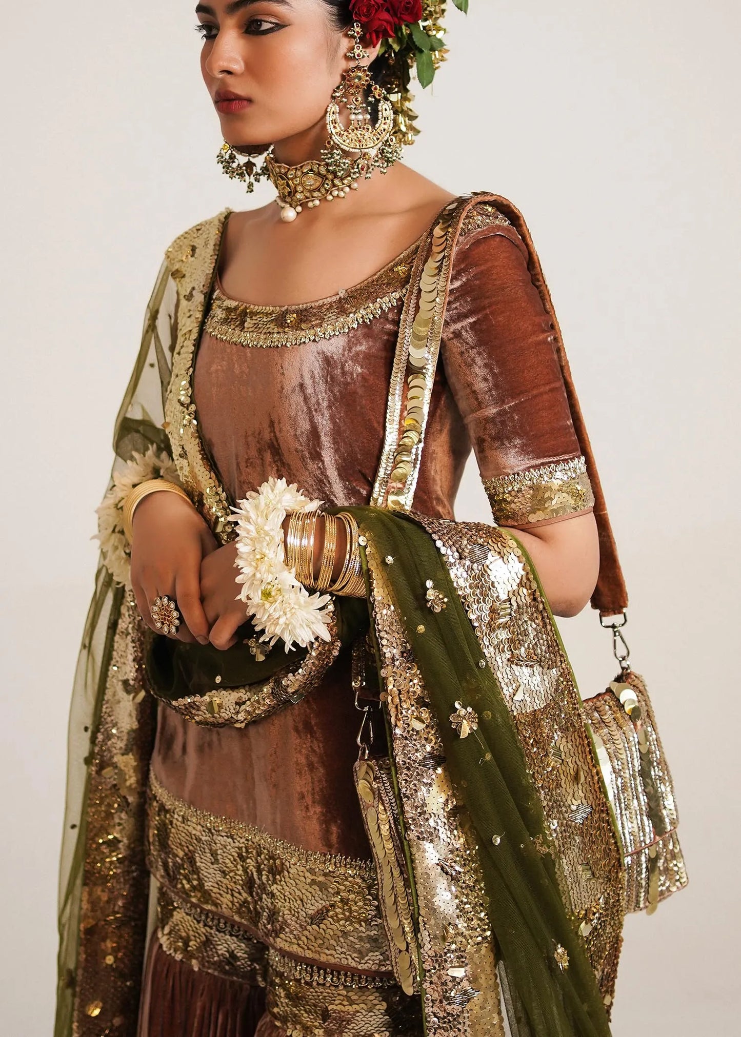 Woman in traditional attire with gold and brown colors, holding a white flower.