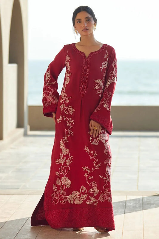 Woman wearing a red embroidered dress standing in a bright room with large windows.
