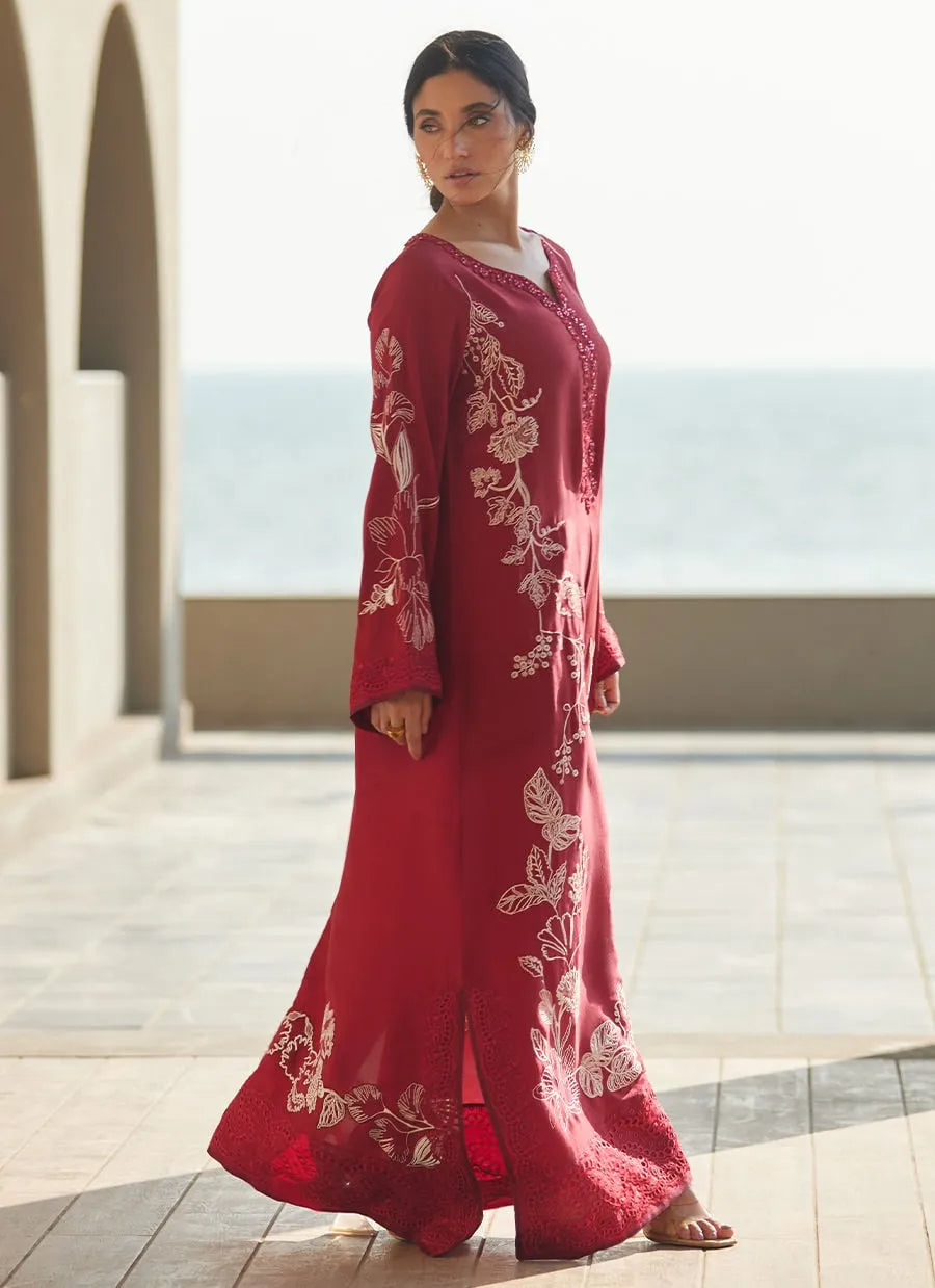 Woman wearing a red embroidered dress standing in an outdoor setting with arches and a blurred background.