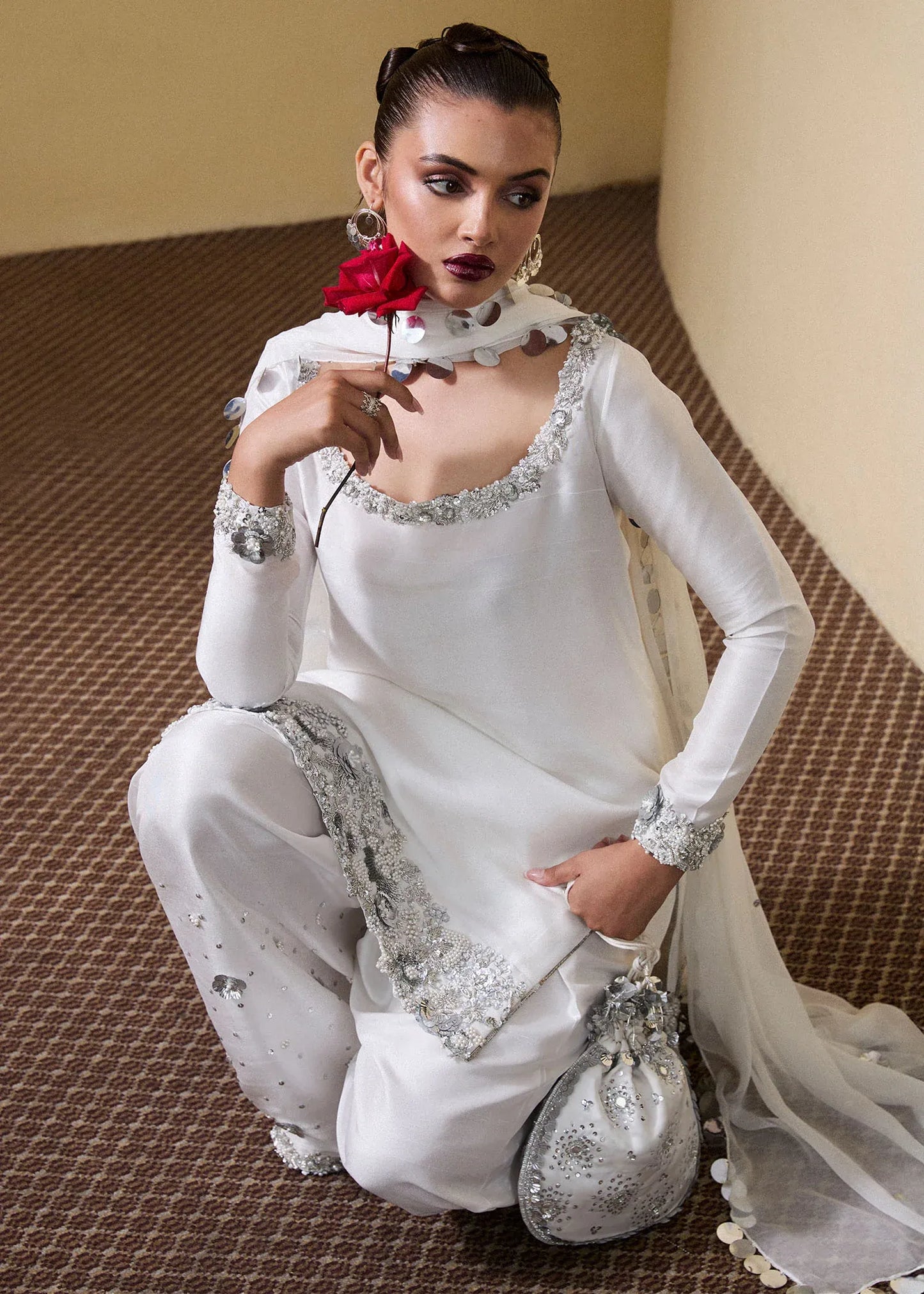 Woman in a white traditional outfit with silver embroidery, holding a matching handbag.