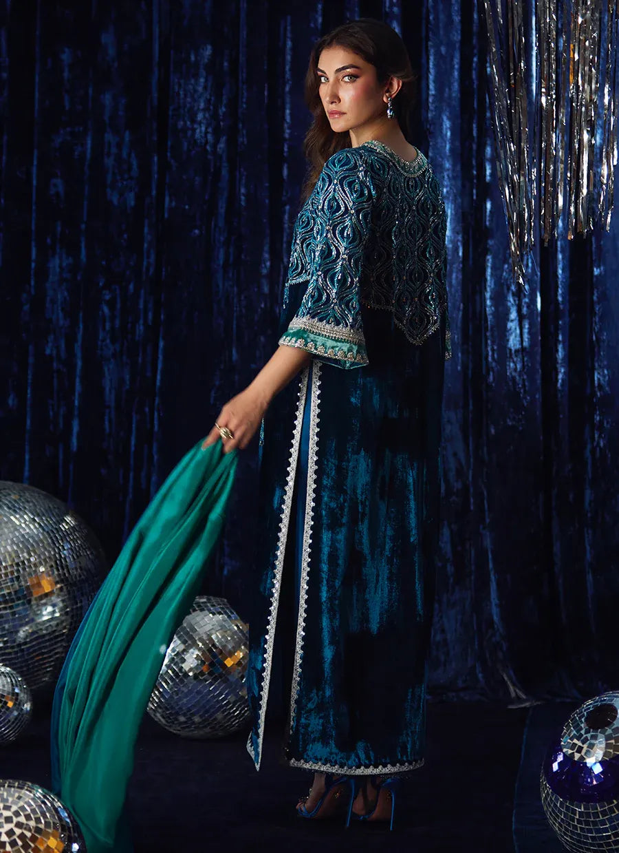 Woman in a blue embroidered outfit holding a green fabric against a dark background with disco balls.