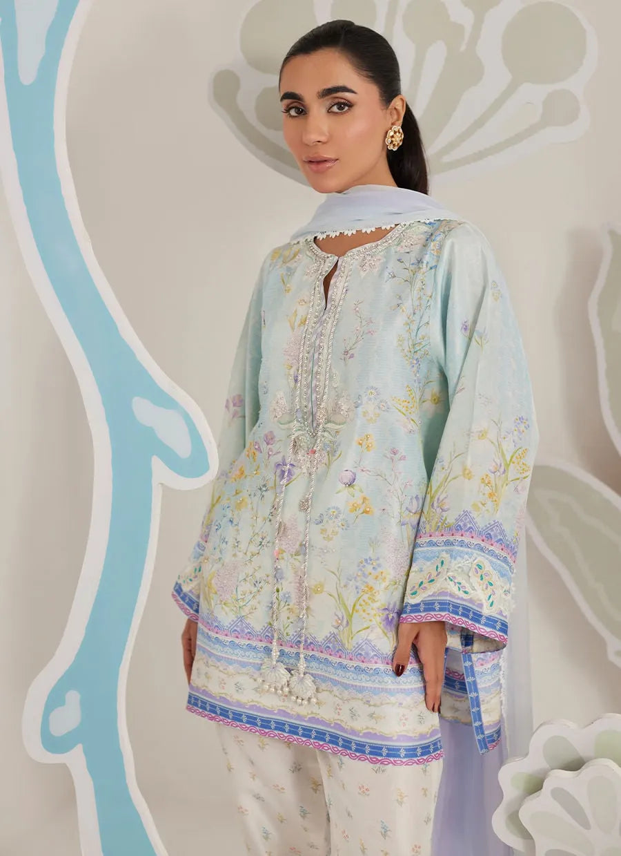 Woman wearing a light blue embroidered shirt with a floral pattern against a decorative background