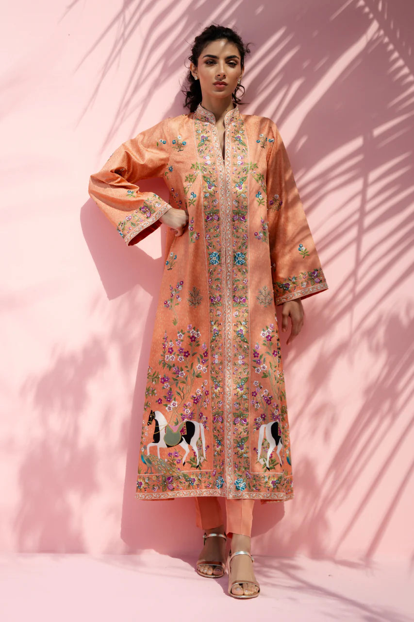 Woman wearing a peach embroidered traditional outfit against a pink background