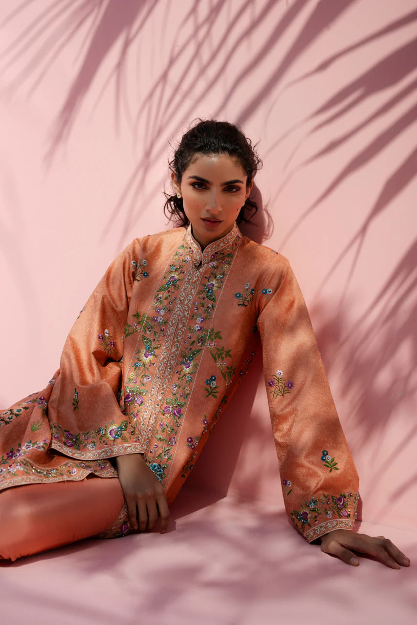 Woman wearing a peach embroidered traditional outfit against a pink background