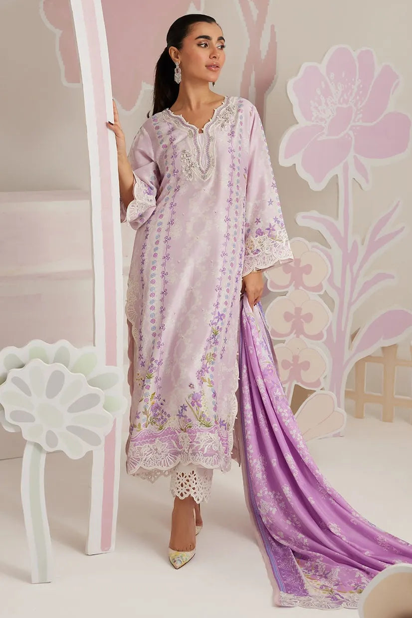 Woman in a light pink embroidered outfit with a purple dupatta against a floral decorated wall.