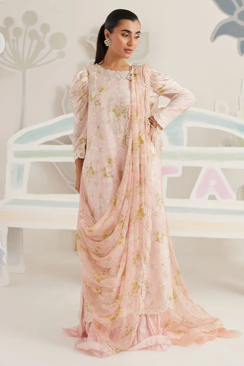 Woman in a floral dress with a matching dupatta against a decorative wall.