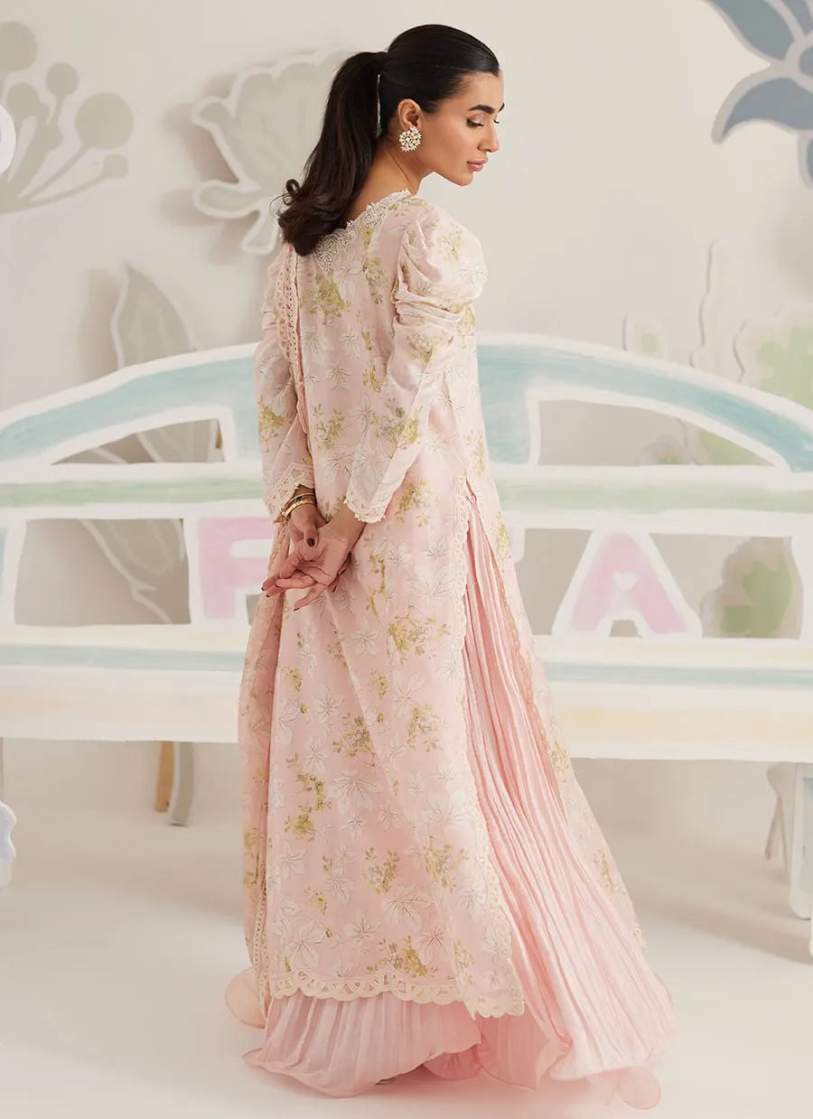 Woman in a light pink floral dress standing in front of a decorative wall with pastel colors.