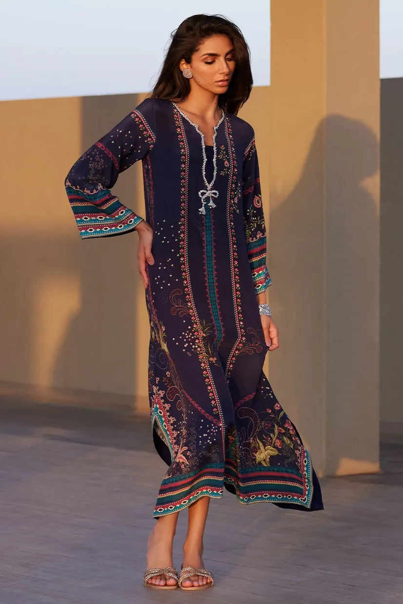 Woman wearing a long, patterned dress standing against a plain background