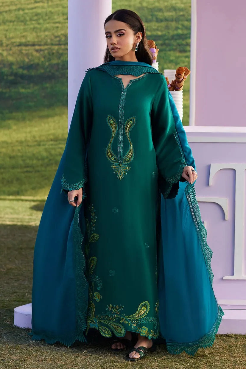 Woman in a long teal dress with green embroidery standing outdoors.