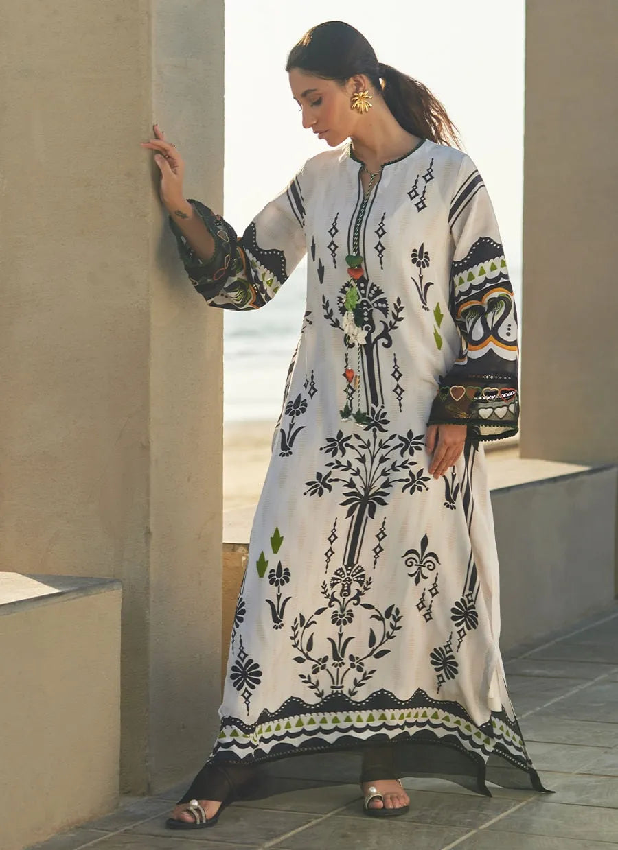 Woman wearing a long, patterned dress standing against a neutral wall.