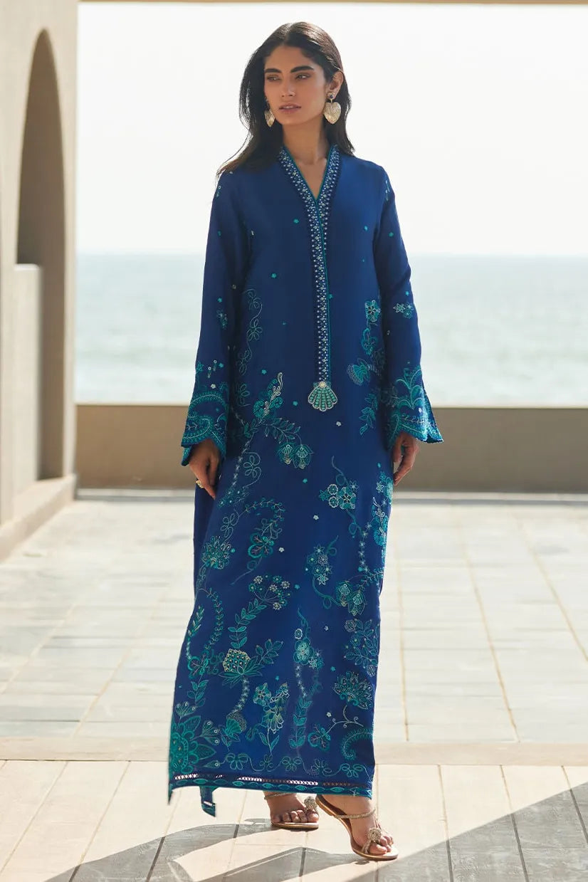 Woman wearing a blue embroidered dress standing on a rooftop with ocean view