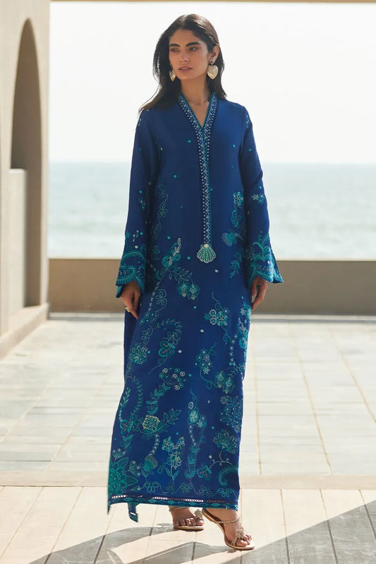 Woman wearing a blue embroidered dress standing on a rooftop with ocean view