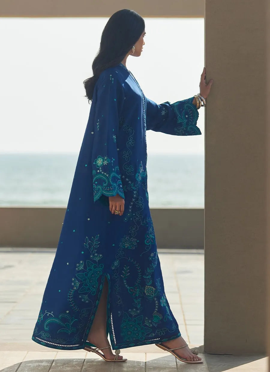 Woman in a blue dress with green patterns standing by a railing with a scenic view.