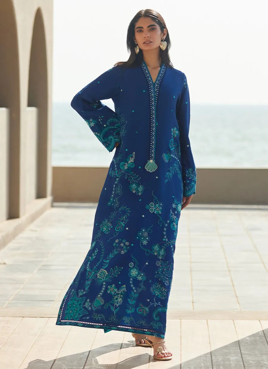 Woman wearing a blue dress with green patterns standing outdoors.